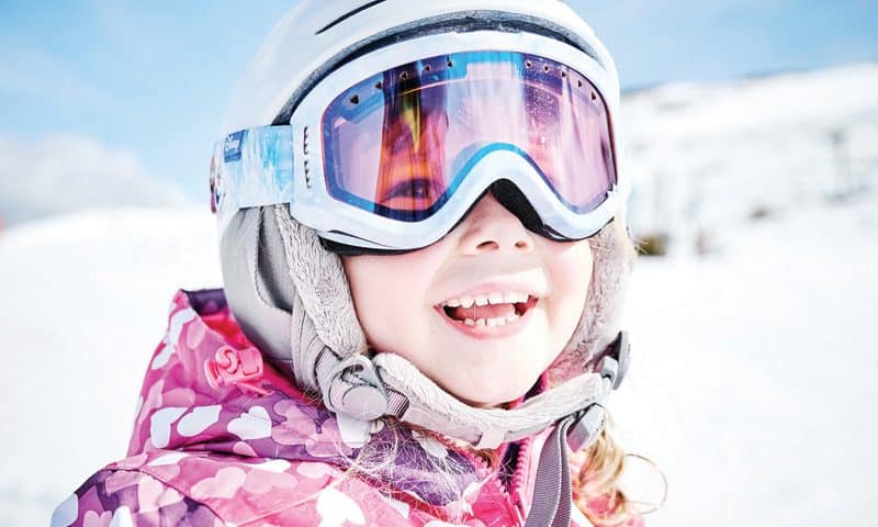 Little kid in ski clothing wearing a helmet and goggles