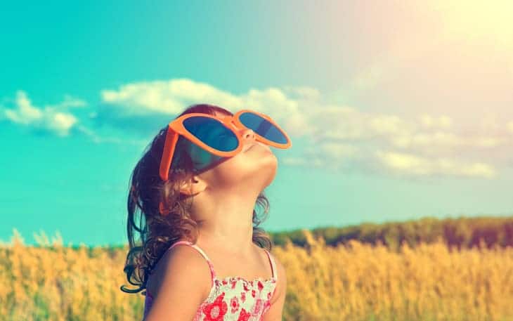 Little girl wearing oversize novelty sunglasses looking at the sky.